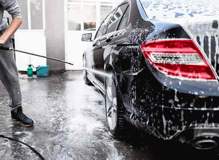 Man washing a black car with pressure washer during professional auto detailing

