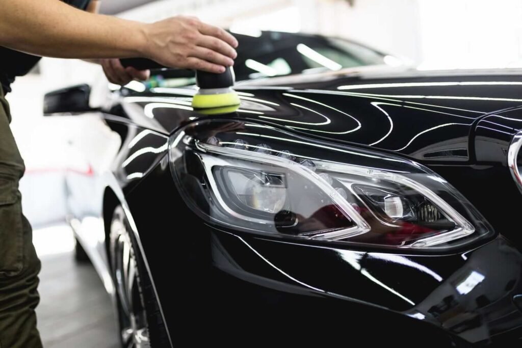 Auto detailer applying car wax on a black luxury car using an orbital buffer
