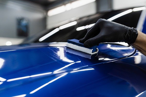 Auto detailer applying ceramic coating on a white car hood