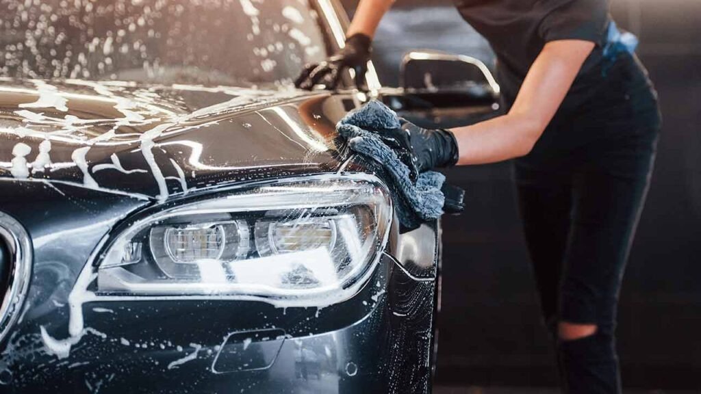 Detailer hand washing a black car with soap and microfiber cloth

