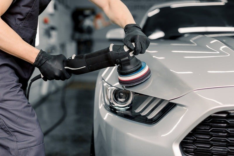 Detailer polishing silver car with orbital polisher in auto shop
