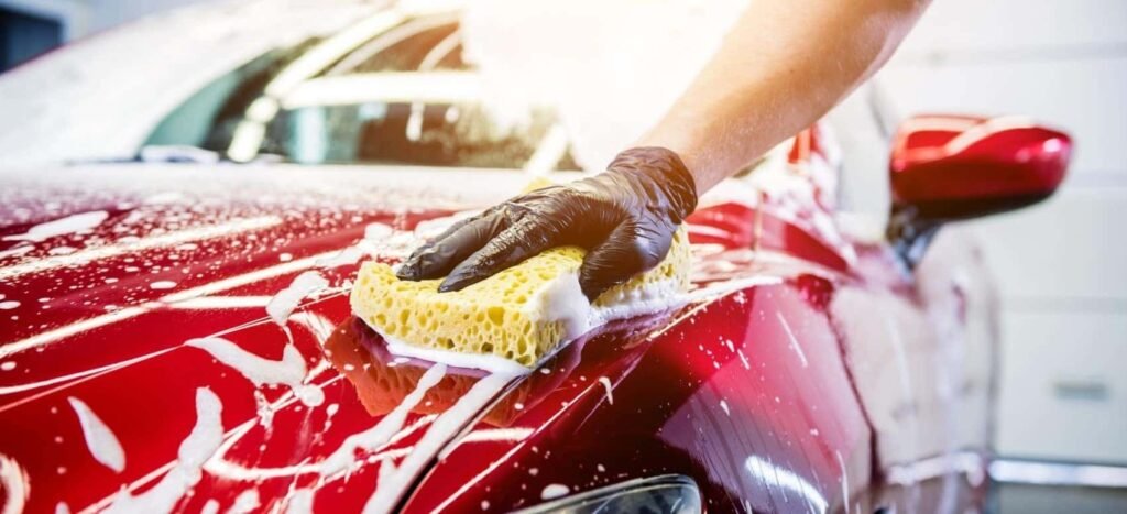 Hand washing a red car with a sponge during a professional car wash in Frisco TX