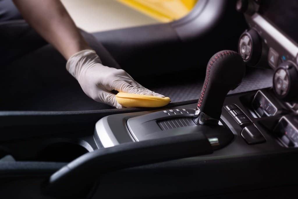 A professional detailer uses a microfiber cloth and cleaning spray to carefully clean the touchscreen display inside a car during an interior detailing session.