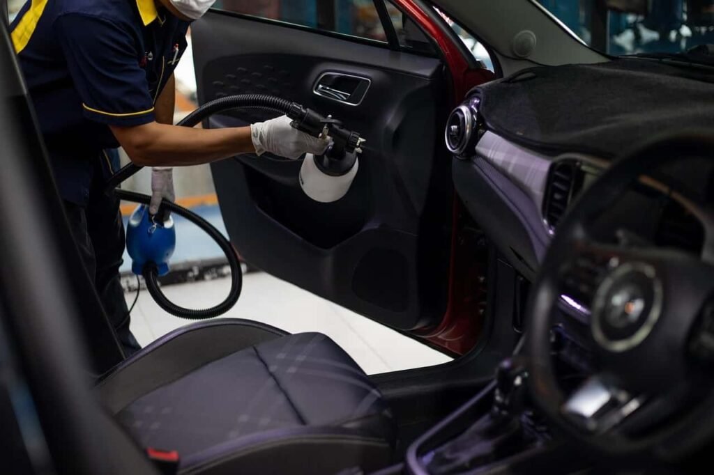 Professional detailer cleaning a car’s touchscreen display with a microfiber cloth and spray bottle during an interior car detailing service.